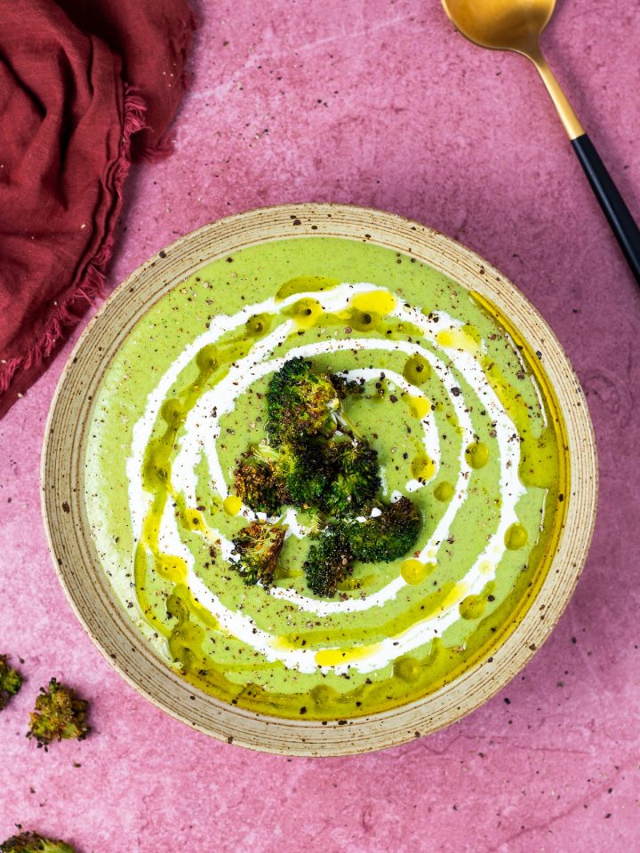 speckled tan bowl filled with a green soup swirled with olive oil and cream