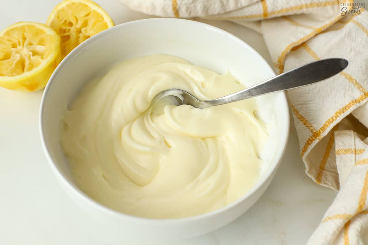 Lemon cream cheese frosting in a white bowl with a spoon in it.