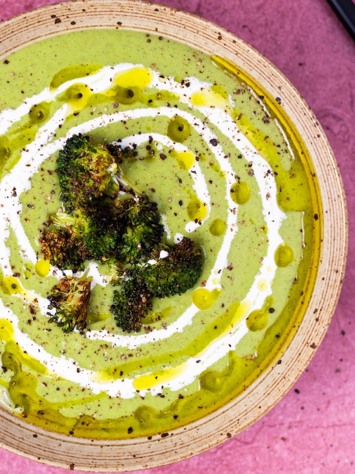 bowl of creamy green soup drizzled with cream and olive oil and topped with roasted broccoli