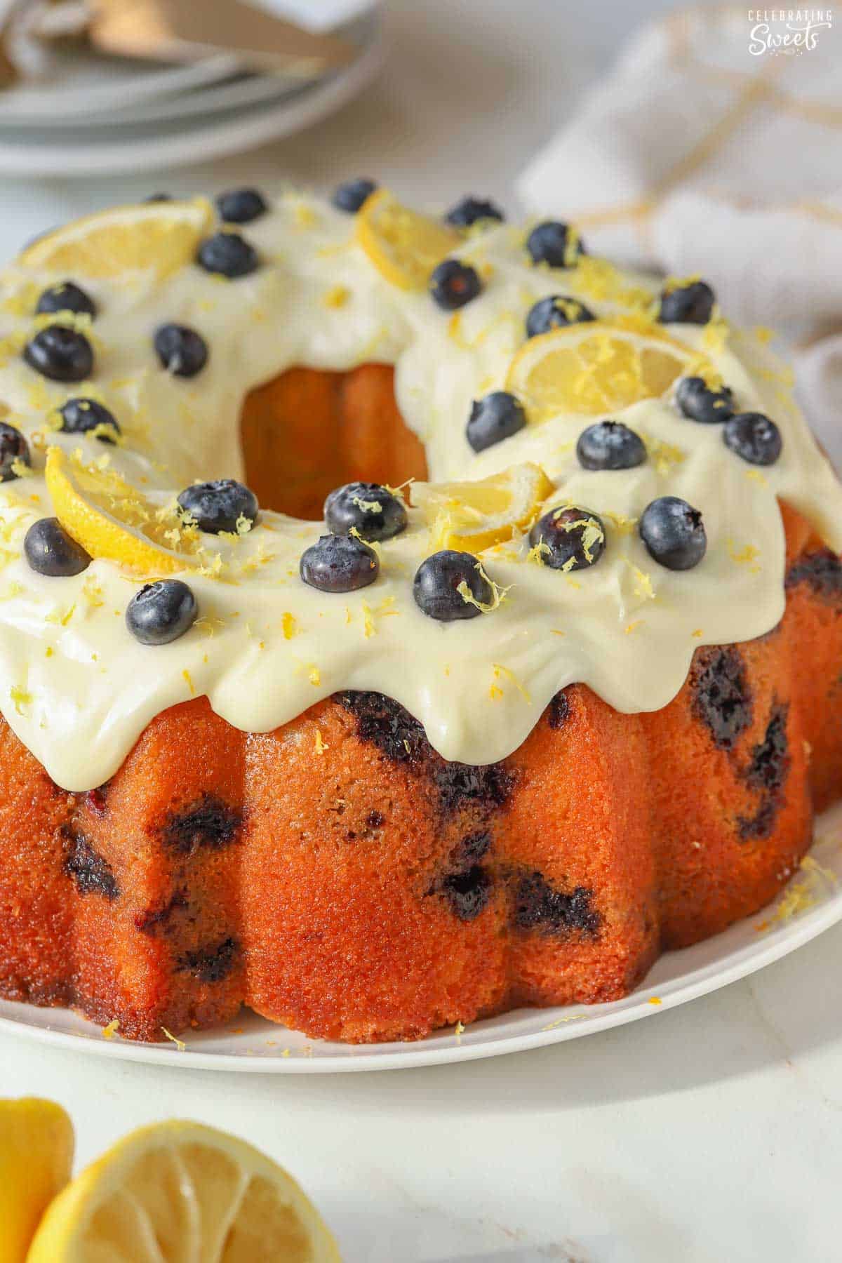 Lemon blueberry bundt cake on a white plate garnished with frosting, blueberries, and lemon slices.