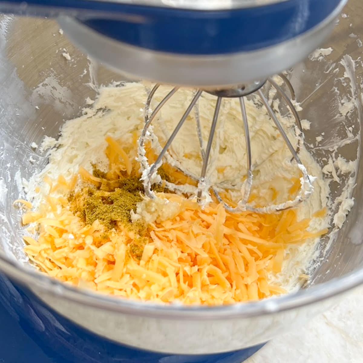 Mixer bowl showing adding the Cheddar cheese, curry and garlic to the cream cheese