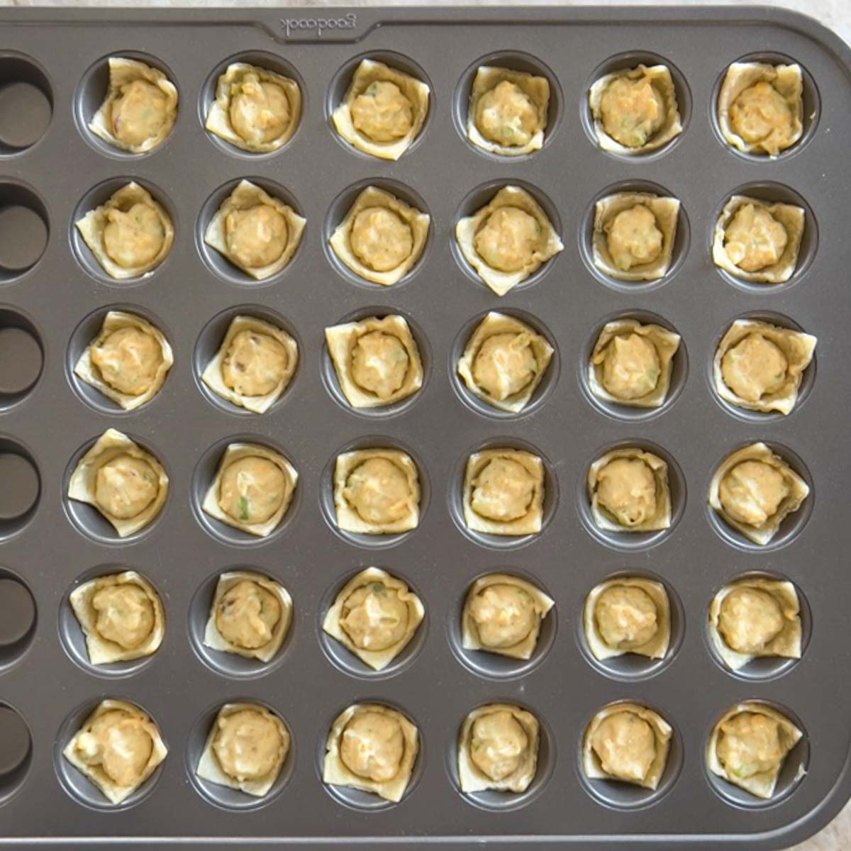 mini muffin tin holding filled puff pastry squares, unbaked
