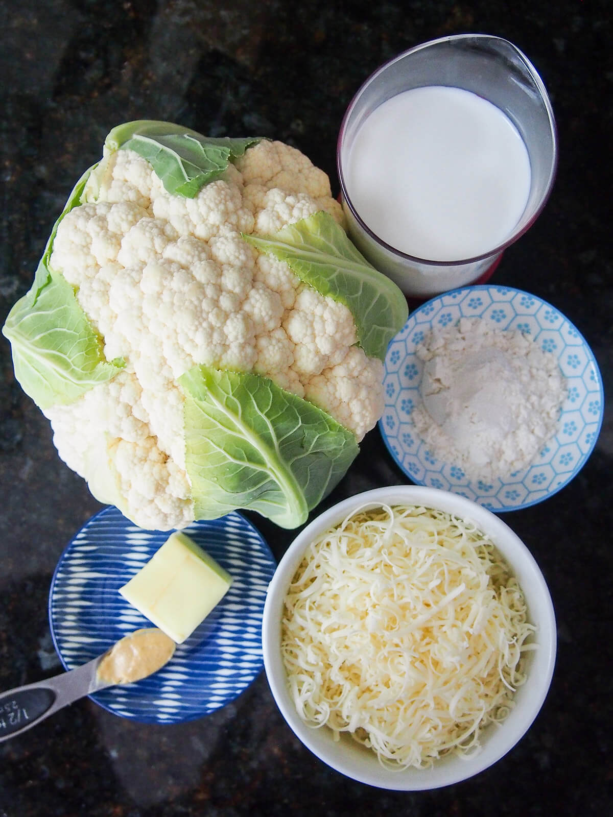Cauliflower, bowl of cheese, flour, milk and dish with butter and mustard