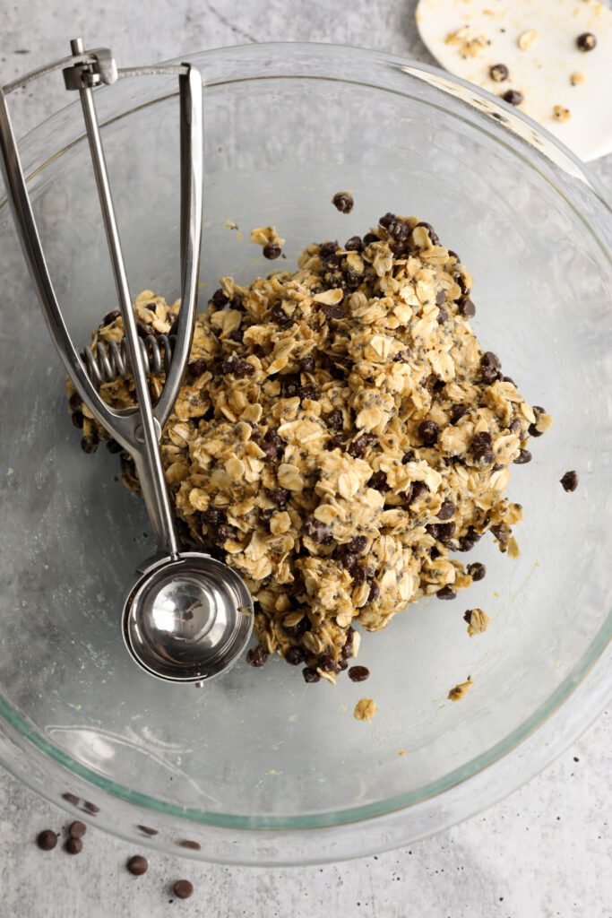 Tahini Chocolate Chip Bliss Ball dough in bowl with cookie scoop and scattered chocolate chips