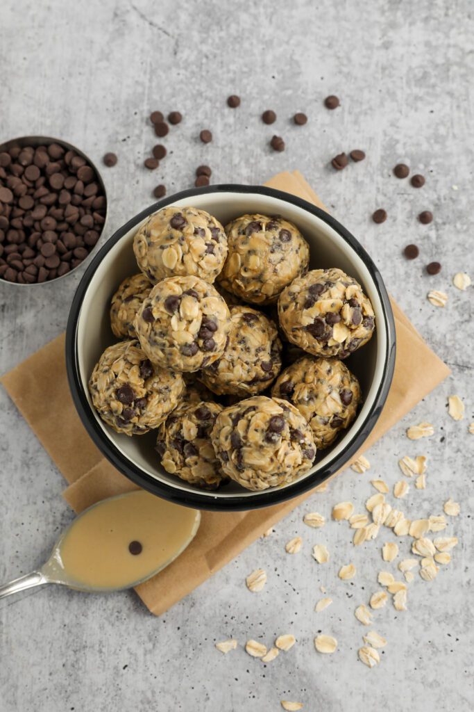 Tahini Chocolate Chip Bliss Balls served in bowl on top of parchment paper with chocolate chips and oats scattered and spoon of tahini 