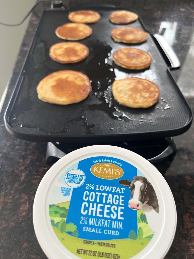 Cottage Cheese Pancakes on a griddle next to a container of cottage cheese