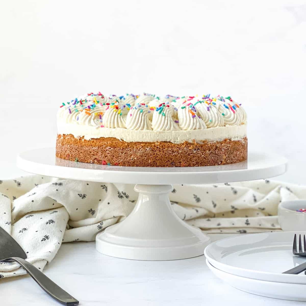 Vanilla Bean Blondie Cheesecake on a white cake stand.