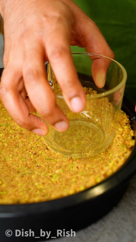 pressing pistachio and biscuit base mixture down into tin