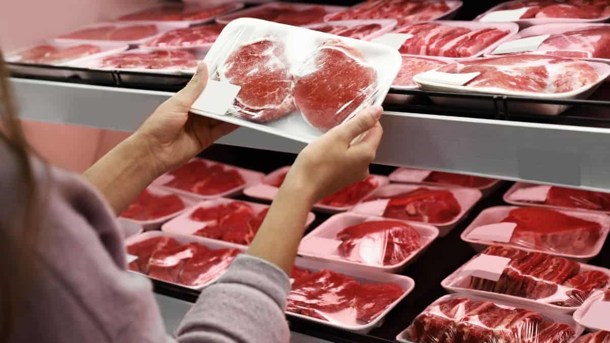 A person selecting packaged meat from a supermarket shelf.
