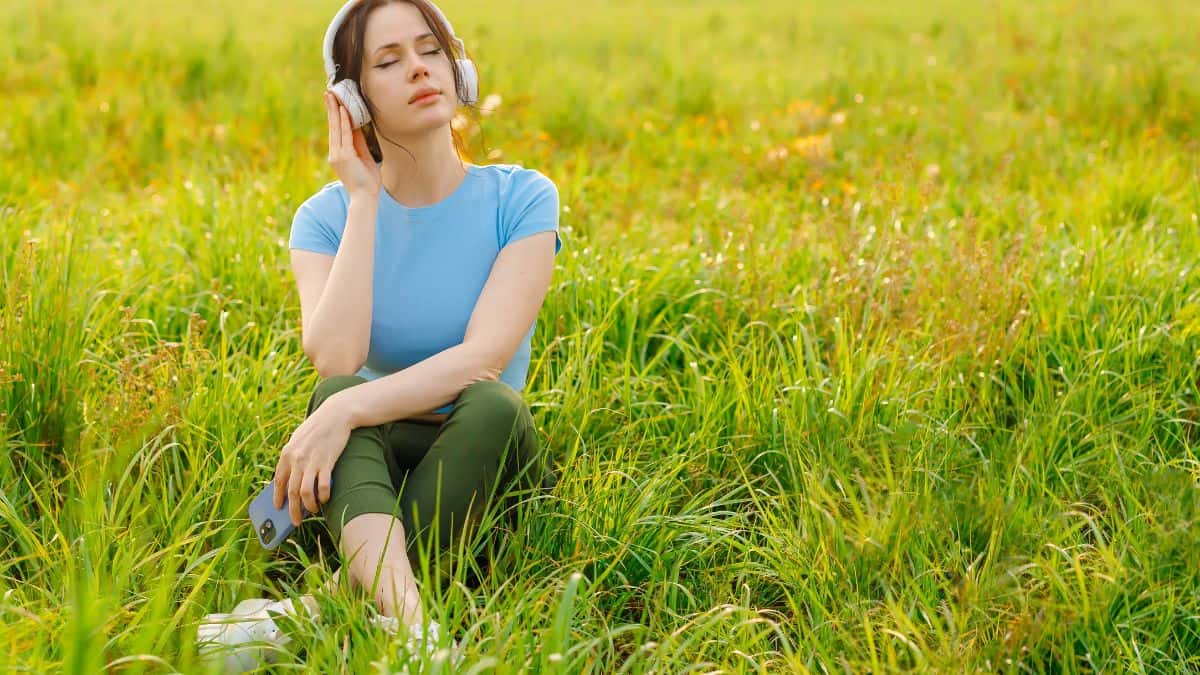 Woman relaxing with headphones in a sunny meadow.