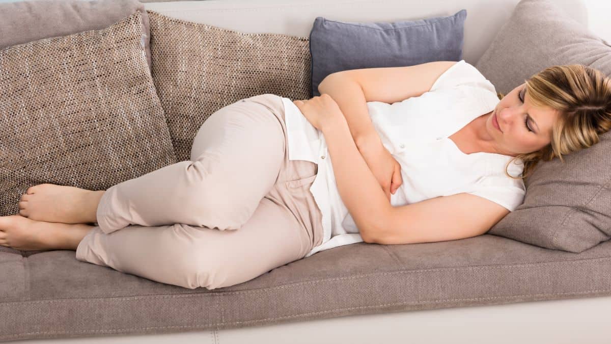 A woman laying on a couch with a stomachache.