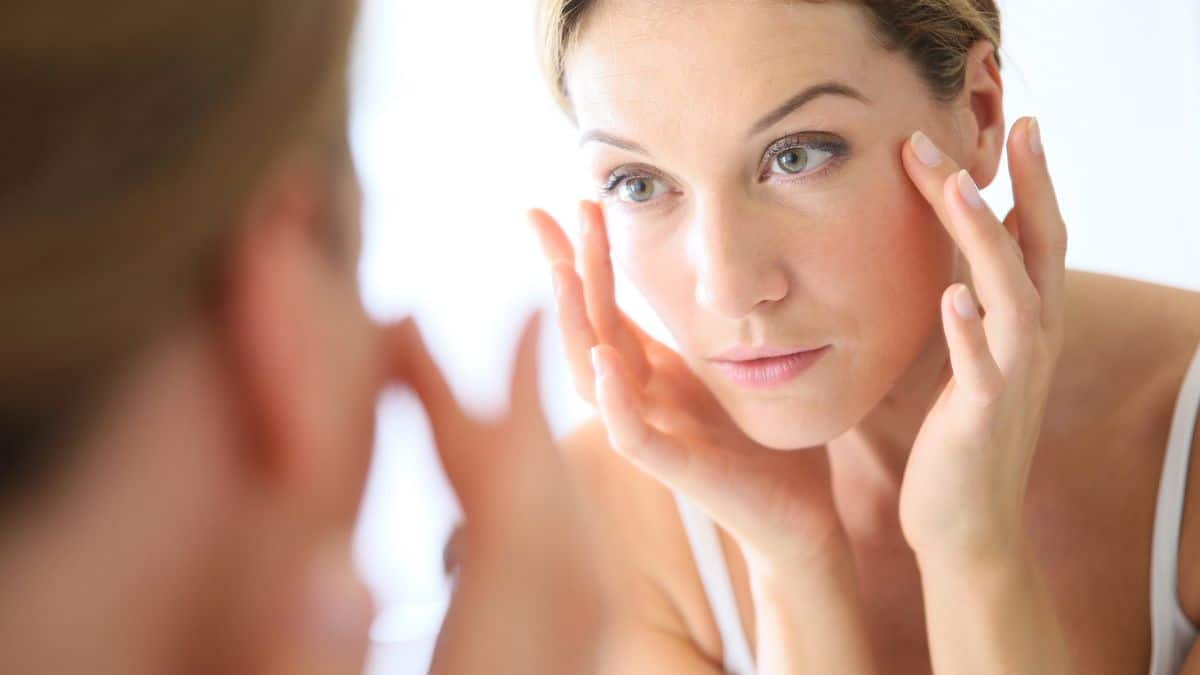 A woman is looking at her face in the mirror, considering foods to look younger.