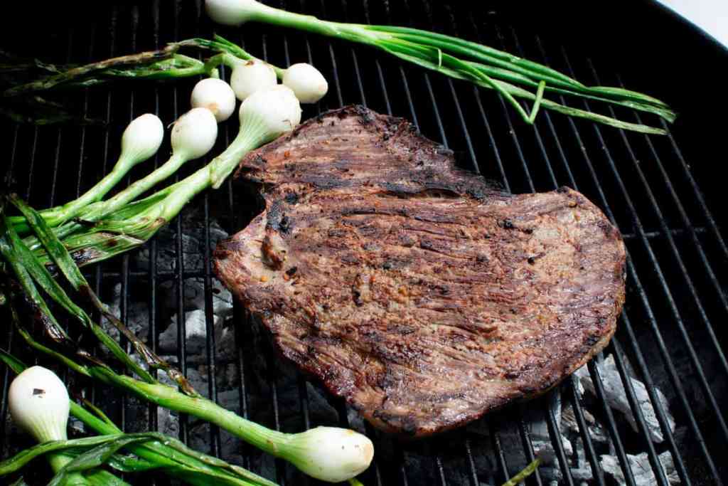 A flank steak and some spring onions on the grill 
