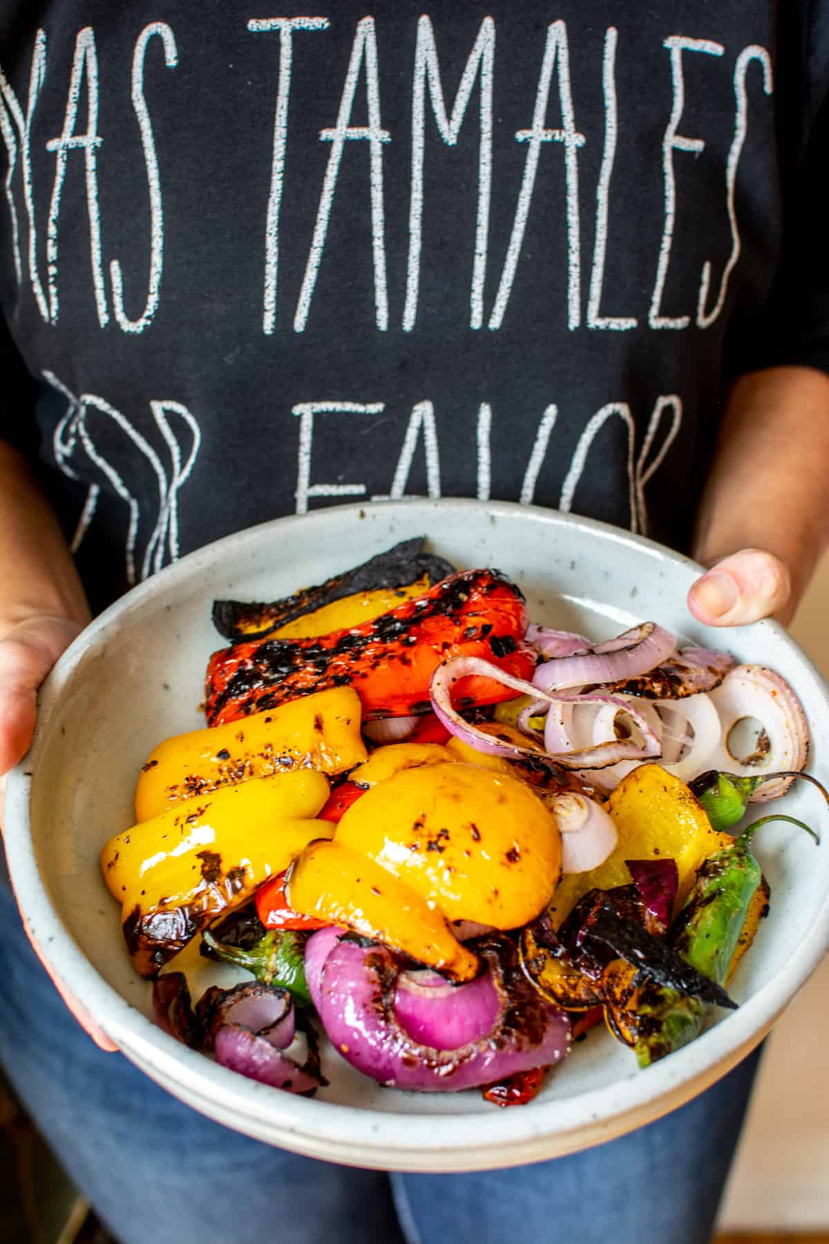 A woman holding a tray of grilled peppers, red onions, grilled serranos, and grilled jalapeños. She is wearing a black sweatshirt. 