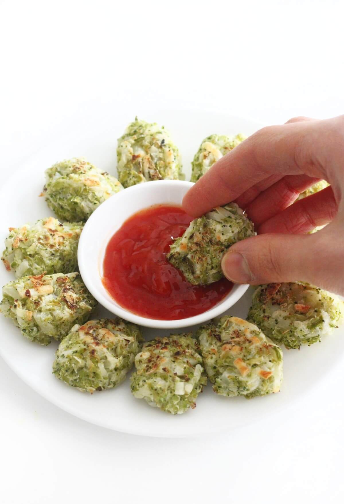 hand dipping broccoli tot in small bowl of ketchup.