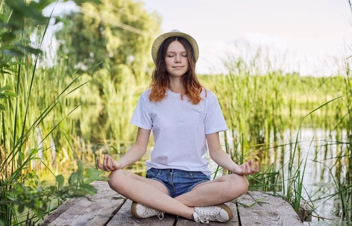 teen meditating on dock near grass and water