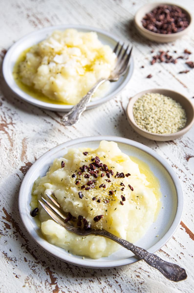 Boiled and mashed yuca with hemp seeds and cocoa nibs on a white plate with a fork.