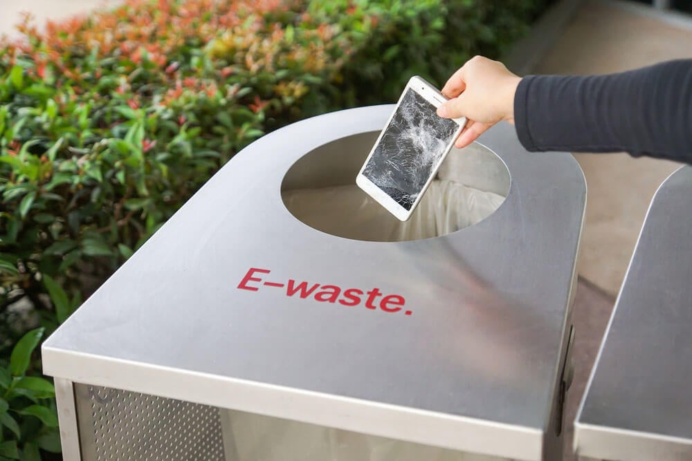 woman placing shattered mobile phone into a bin marked e-waste