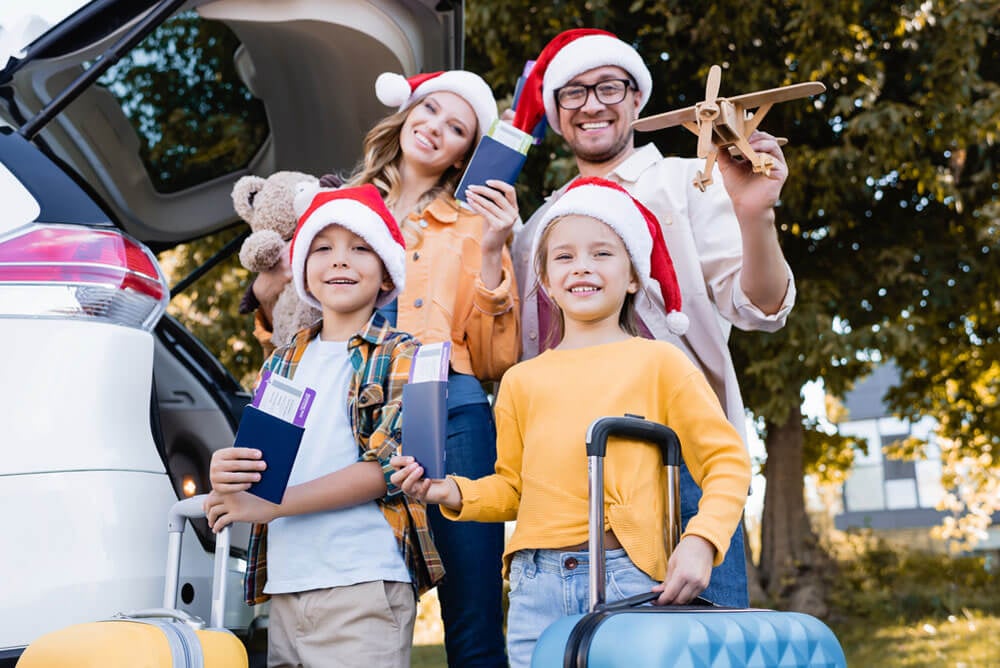 family of four wearing Santa hats, holding suitcases and airplane tickets