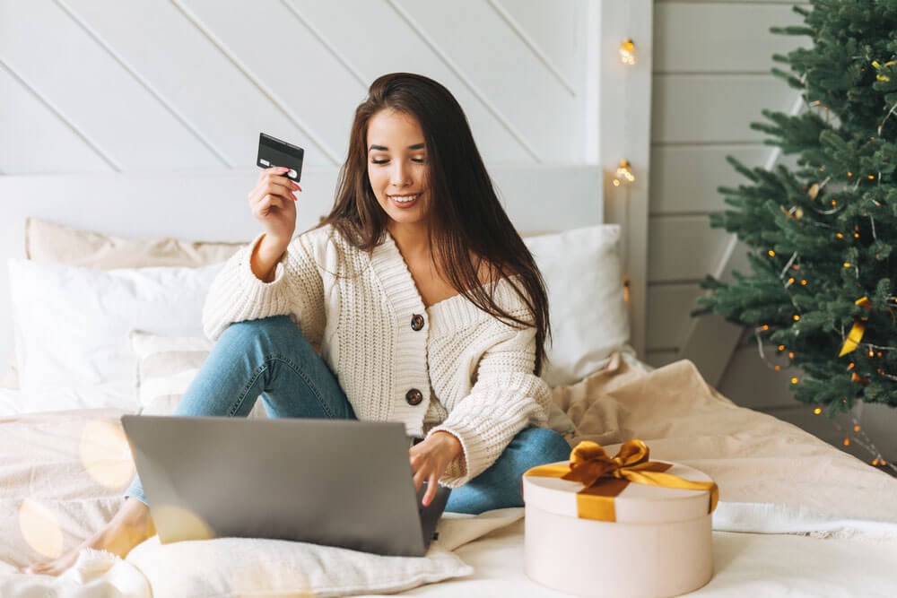 woman with long hair sitting on the bed ordering Christmas gifts online