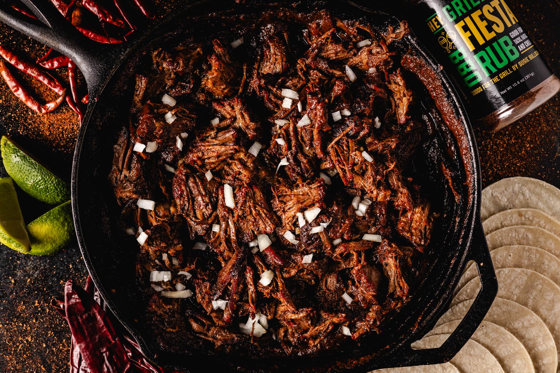 Cooked, shredded barbacoa in skillet next to ingredients.