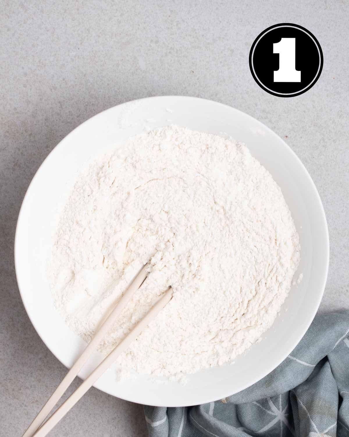 Flour and salt in a bowl with a pair of chopsticks beside.