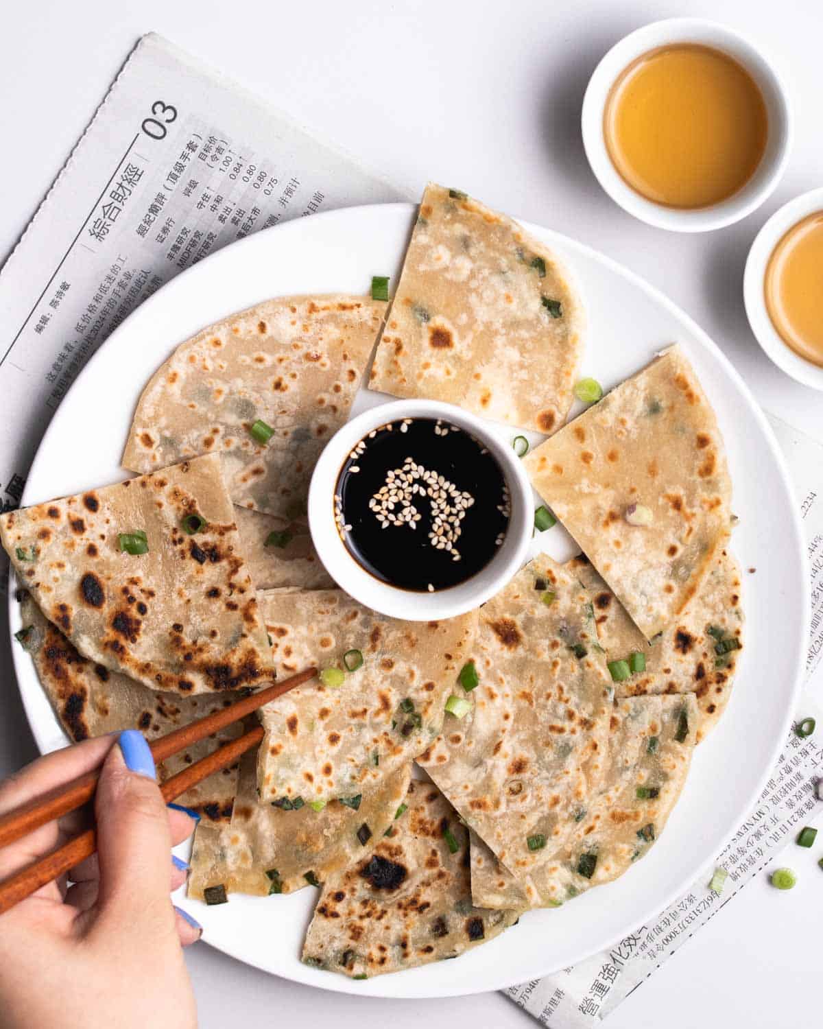A plate of scallion pancake pieces served with soy sauce.