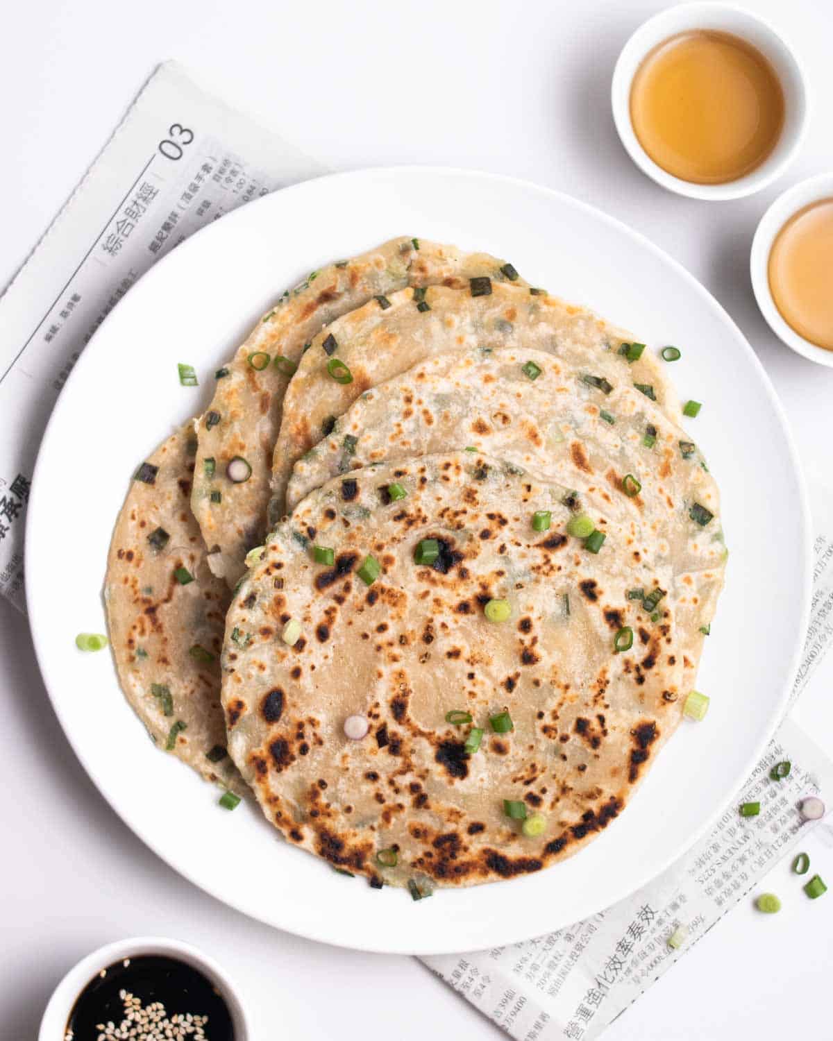 A plate of scallion pancakes with 2 cups of tea beside.