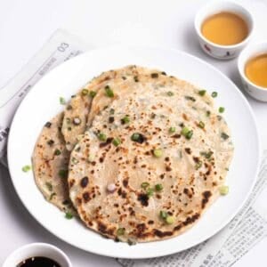 A plate of scallion pancakes topped with chopped green onion with 2 cups of tea in the background.