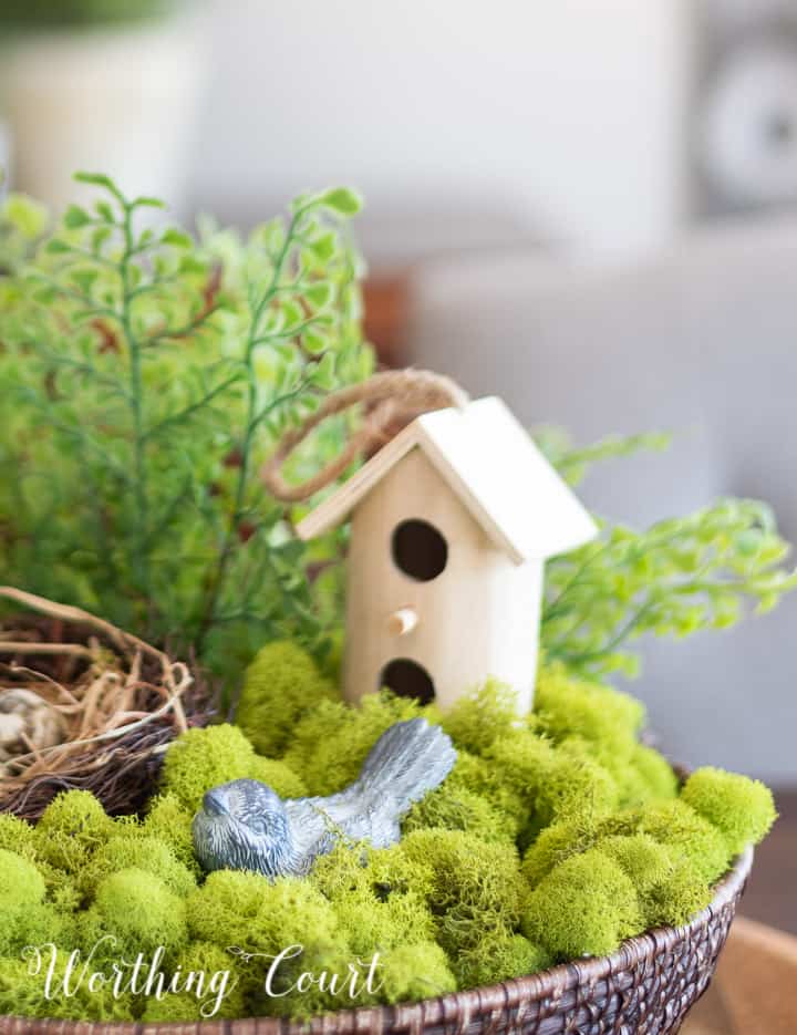wicker bowl filled with green moss, faux greenery, a nest and faux bird