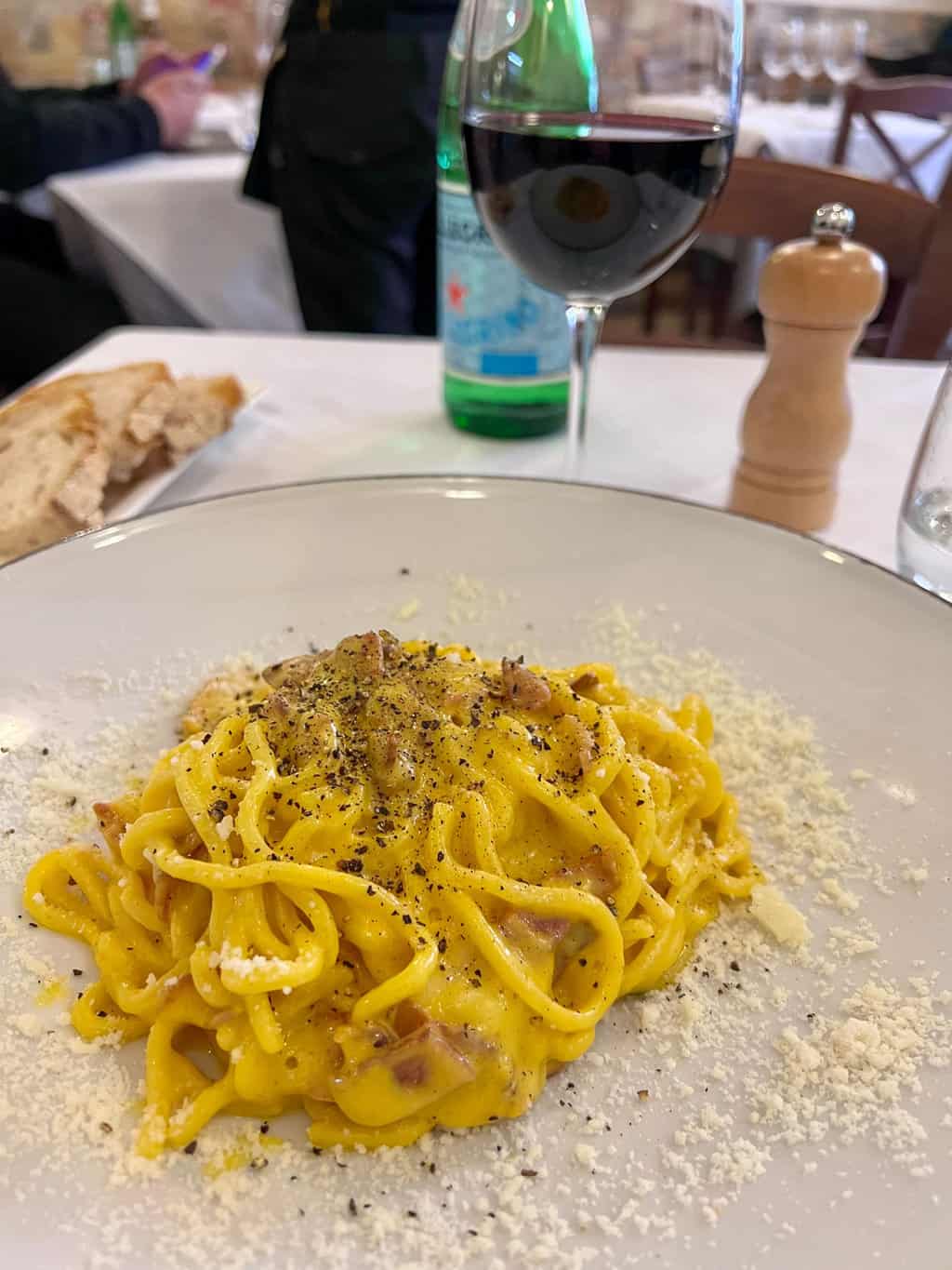A plate of traditional carbonara pasta with a glass of red wine in a restaurant in Rome. Food and wine tour