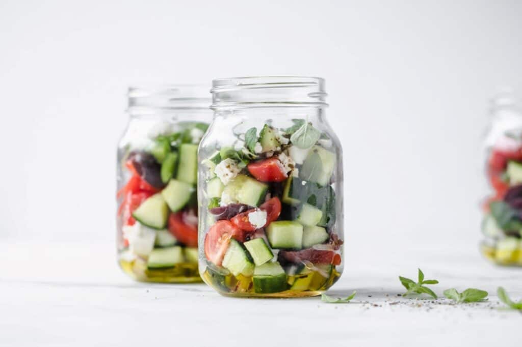 Greek salad meal prep jars on a marble countertop.